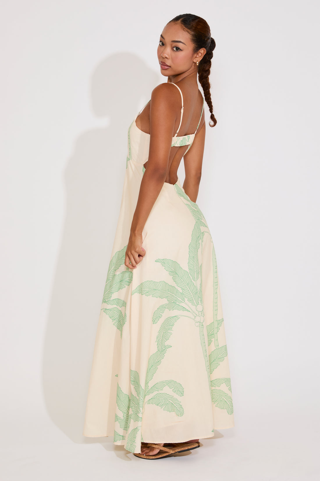 Woman wearing a cream dress with green palm leaf pattern against a white background