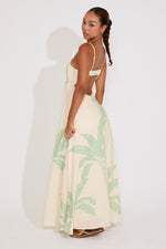 Woman wearing a long, light-colored dress with green leaf patterns on a white background