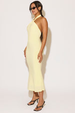 Woman wearing a light yellow halter neck dress against a white background