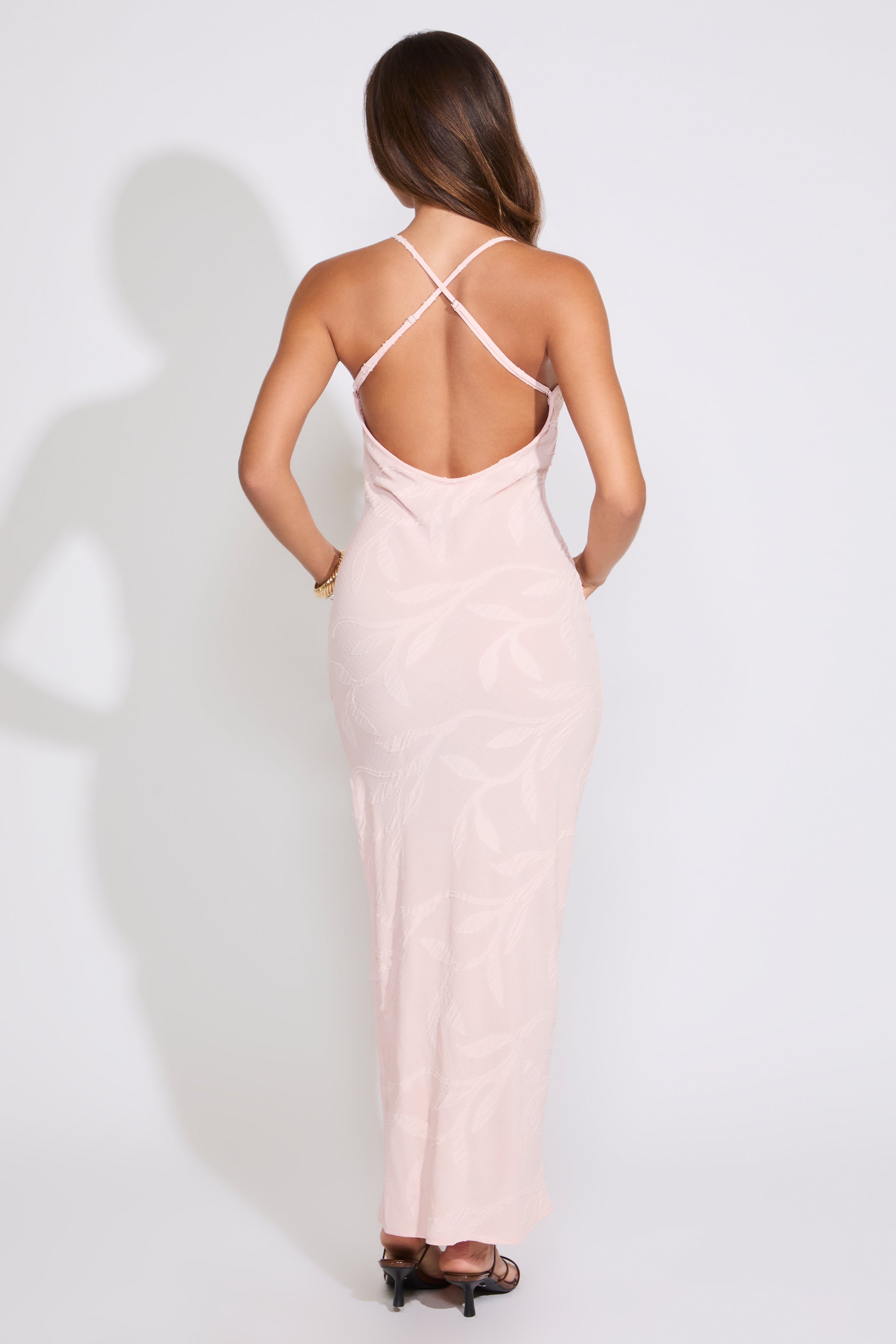 Model is wearing a blush TEXTURED VINE DETAIL CROSS BACK MAXI DRESS with brown heels on a white background.