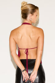Woman wearing a burgundy halter top with thin straps and a black leather skirt on a white background