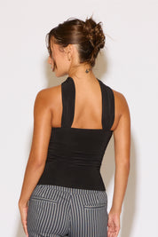 Woman wearing a black sleeveless top and gray striped pants against a white background