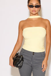 Woman wearing a light yellow strapless top and striped pants against a white background