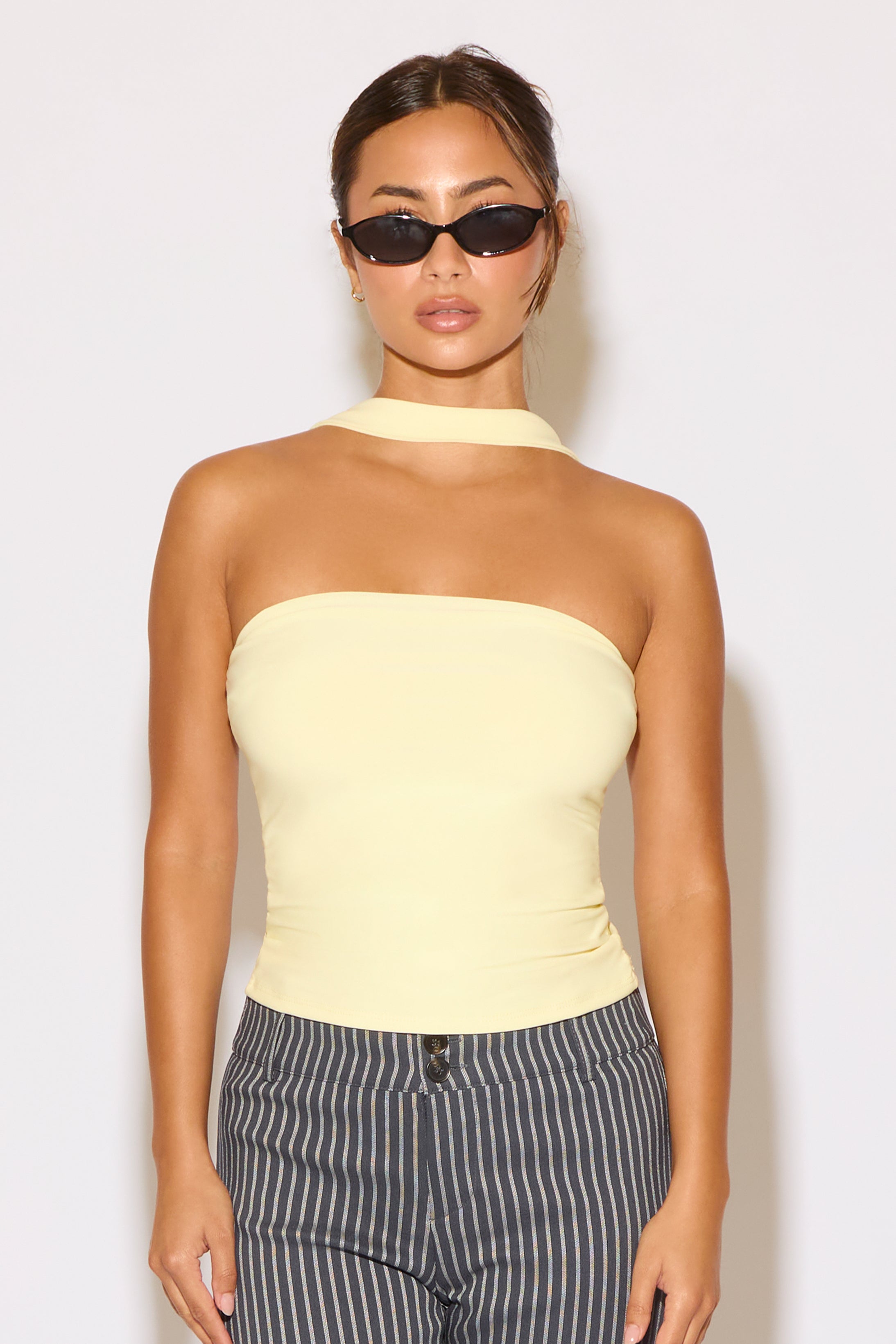 Woman wearing a light yellow strapless top and striped pants against a white background