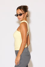 Woman wearing a light yellow sleeveless top and striped pants against a white background
