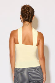 Woman wearing a light yellow sleeveless top and striped pants against a white background