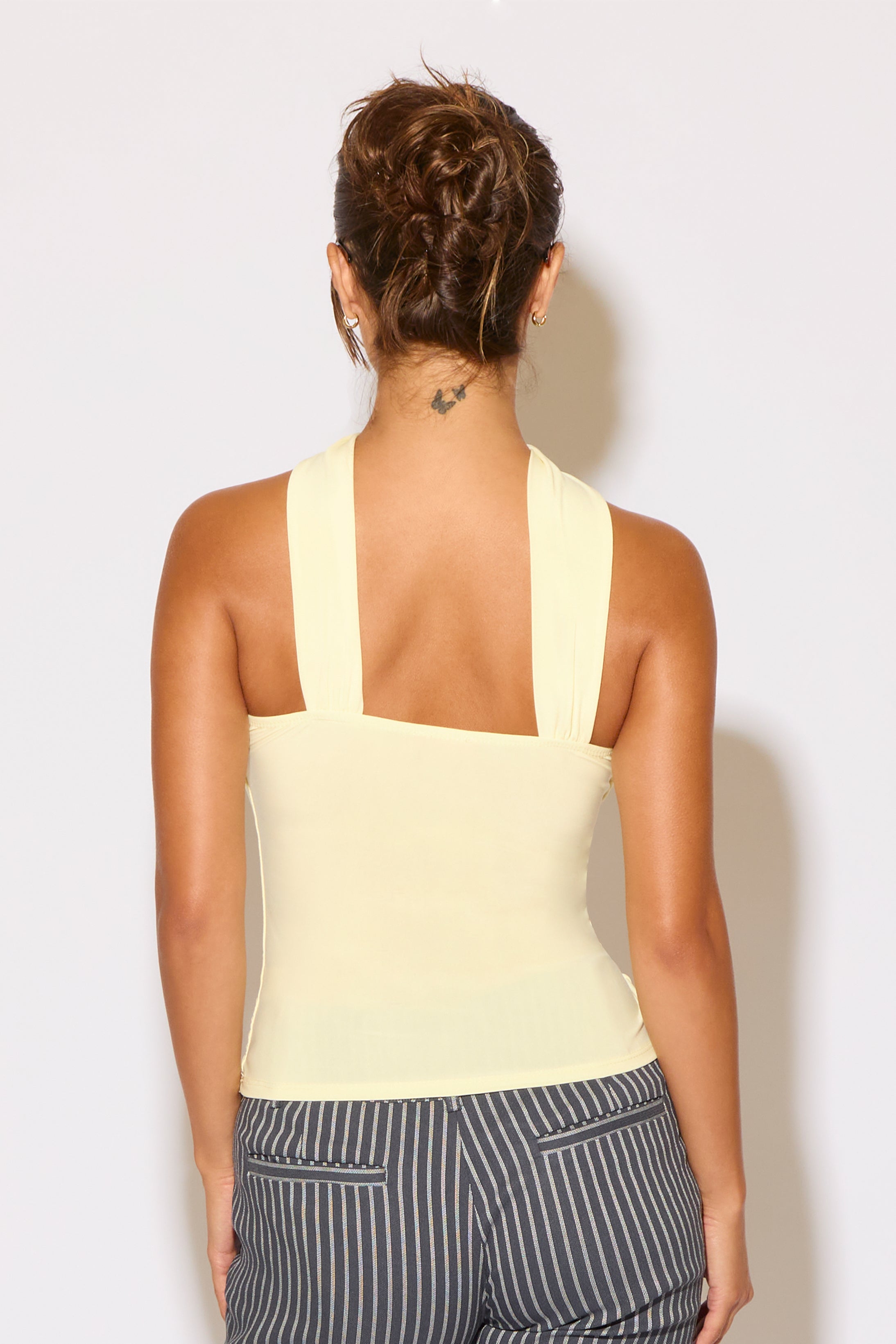 Woman wearing a light yellow sleeveless top and striped pants against a white background