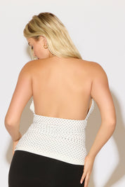 Model is wearing a white low cut polka dot halter top with a black skirt on a white background.