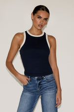 Woman wearing a black tank top and blue jeans against a plain background