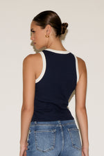 Woman wearing a navy tank top with white trim and blue jeans against a plain background