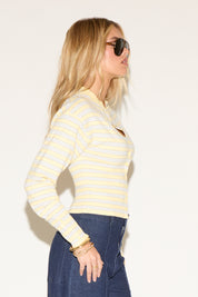 A woman in sunglasses wearing a yellow striped sweater and high-waisted wide-leg jeans poses confidently against a plain white background.