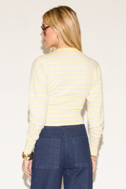 A woman in sunglasses wearing a yellow striped sweater and high-waisted wide-leg jeans poses confidently against a plain white background.