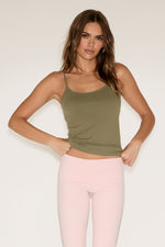 Woman wearing a green tank top and pink leggings against a white background