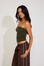Woman wearing a green strapless top and brown pants against a white background