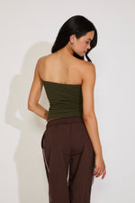 Woman wearing a strapless green top and brown pants against a white background