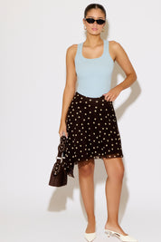 Woman wearing a light blue sleeveless top and black polka dot skirt on a white background