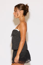 Woman wearing a black polka dot top with lace trim on a white background