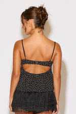 Woman wearing a black polka dot top with cut-out design on a white background