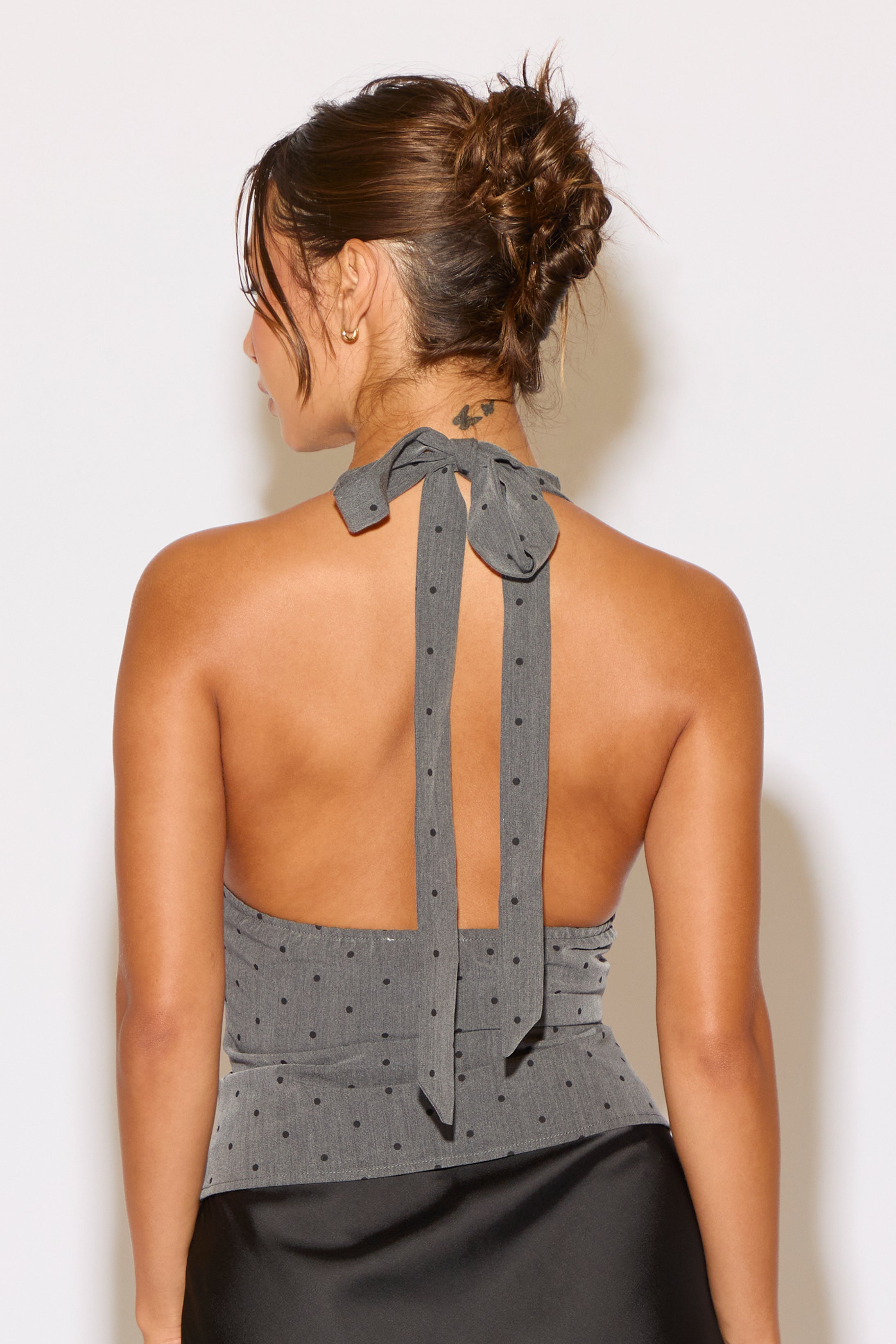 Woman wearing a gray halter top with a bow detail on a white background