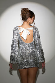 Silver sequin dress with a white bow on the back against a gray background