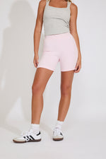 Person wearing a gray tank top and pink bike shorts on a white background