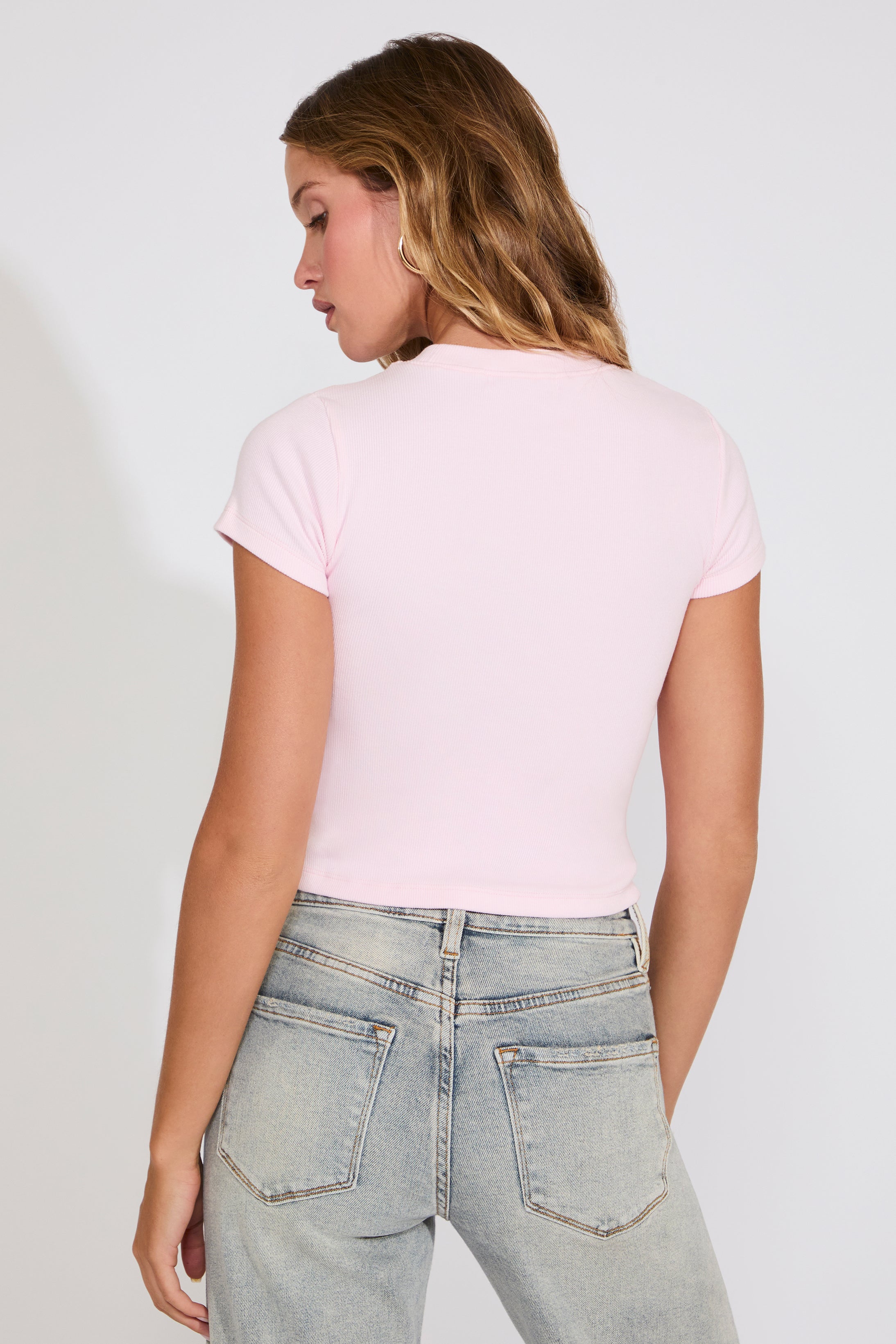 Person wearing a light pink t-shirt and light blue jeans against a plain background