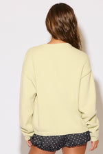 Person wearing a light green sweatshirt and black shorts with white polka dots on a plain background