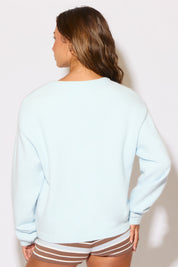 Woman wearing a light blue sweatshirt and striped shorts against a plain background