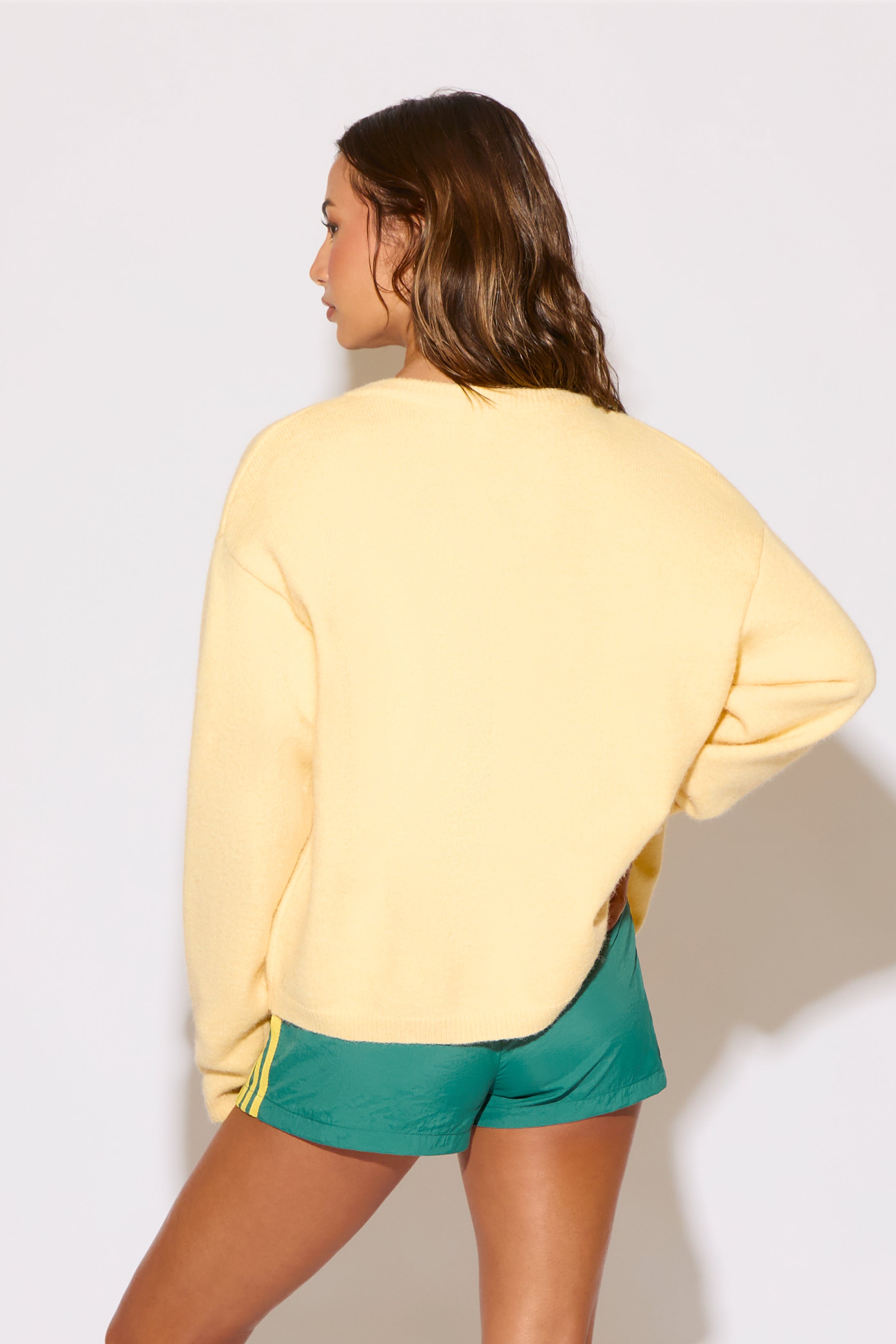 Person wearing a yellow sweatshirt and green shorts against a plain background