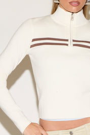 A person poses a white sweater with brown stripes.