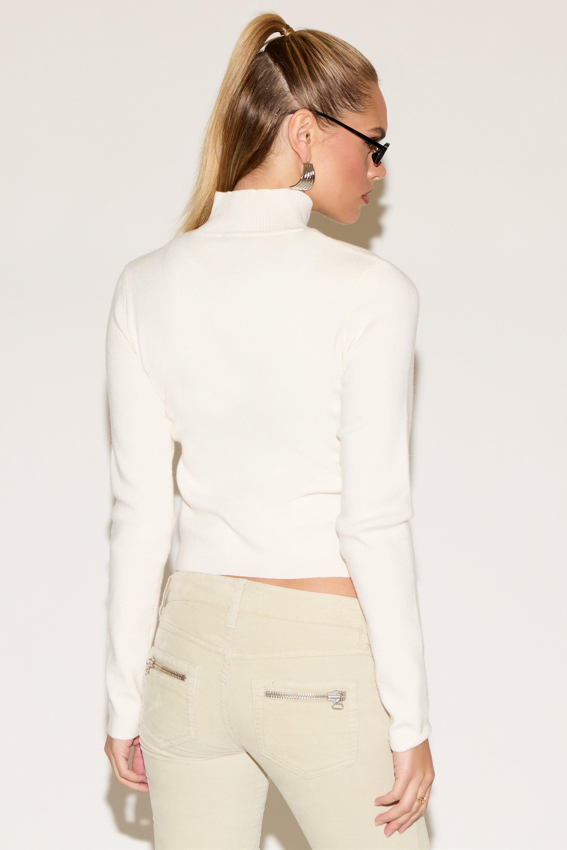 A person poses a white sweater.