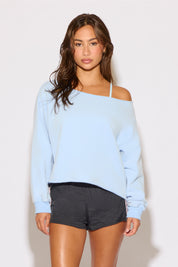 Woman wearing a light blue off-shoulder sweater and black shorts on a white background