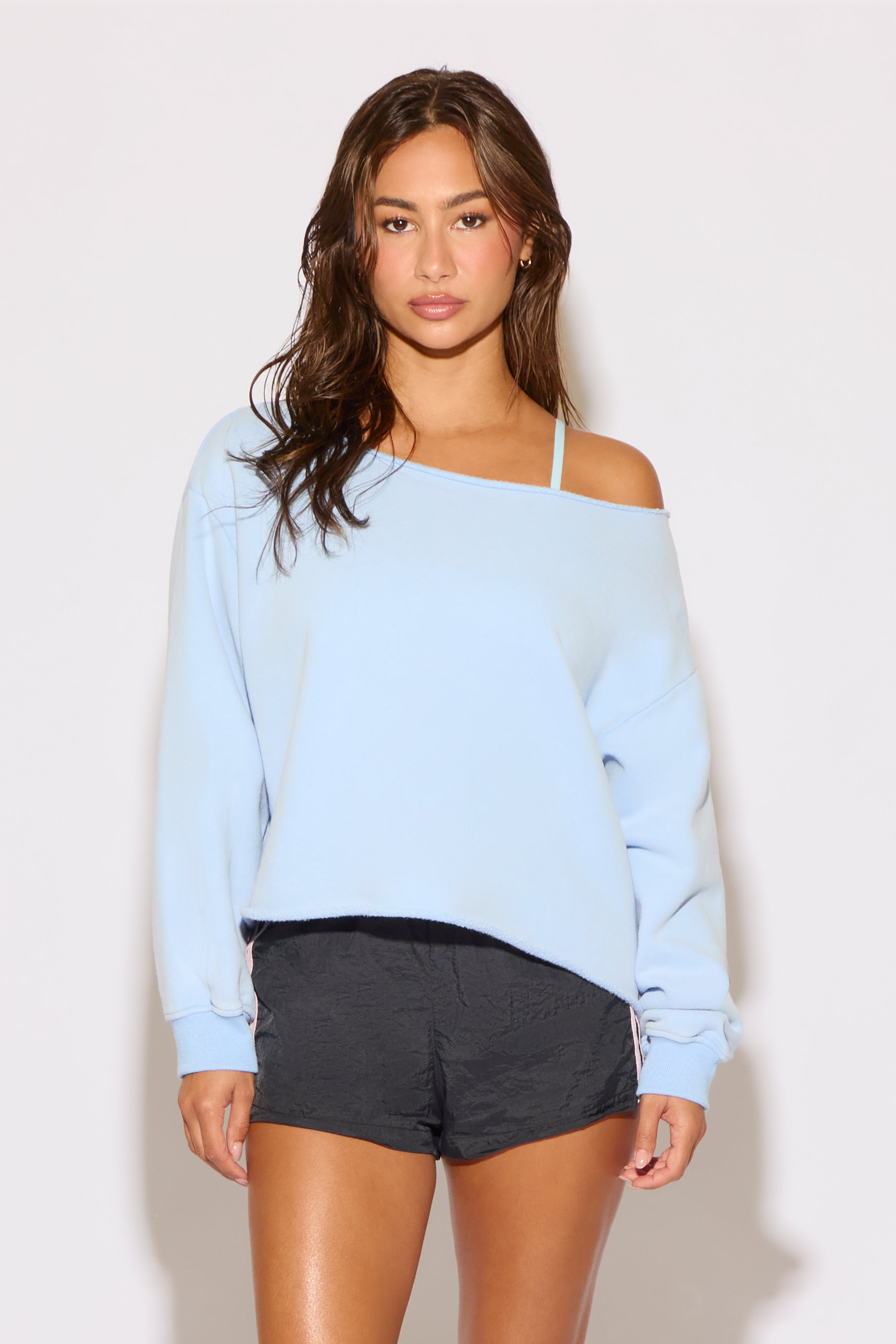 Woman wearing a light blue off-shoulder sweater and black shorts on a white background