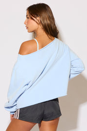 Woman wearing a light blue oversized sweatshirt and black shorts against a plain background