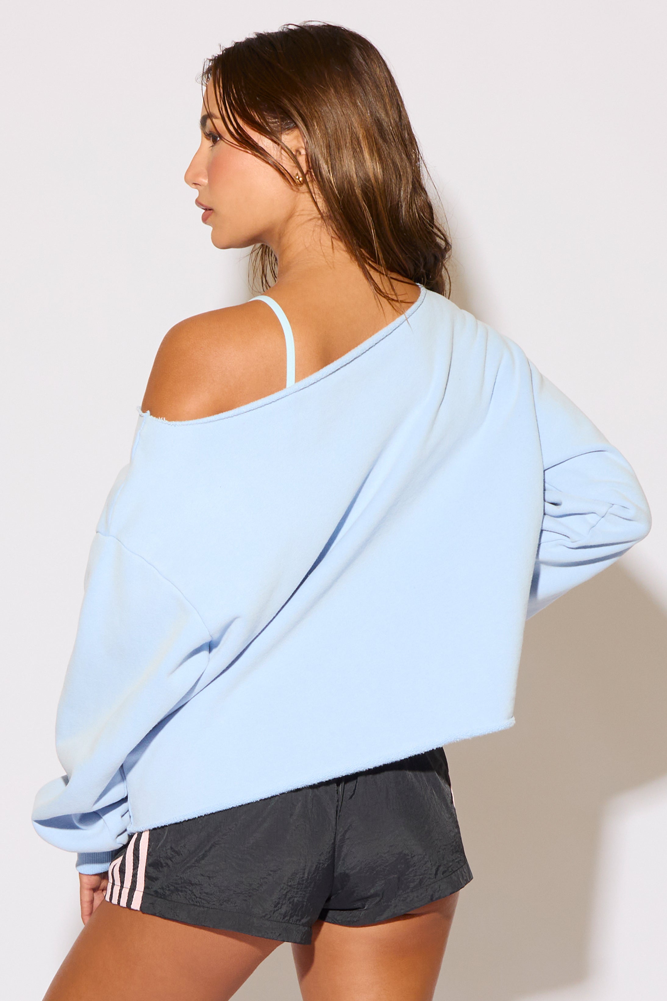 Woman wearing a light blue oversized sweatshirt and black shorts against a plain background