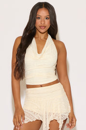 Woman wearing a cream-colored halter top and skirt against a white background