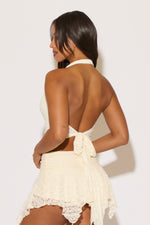 Woman wearing a white lace halter top and skirt against a plain background