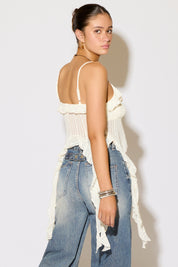 Woman wearing a white lace top and blue jeans against a plain background