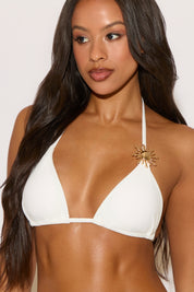 Woman wearing a white bikini with a gold embellishment against a plain background
