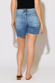 Model is wearing tummy control high rise mid length medium denim shorts with a black top on a white background. 