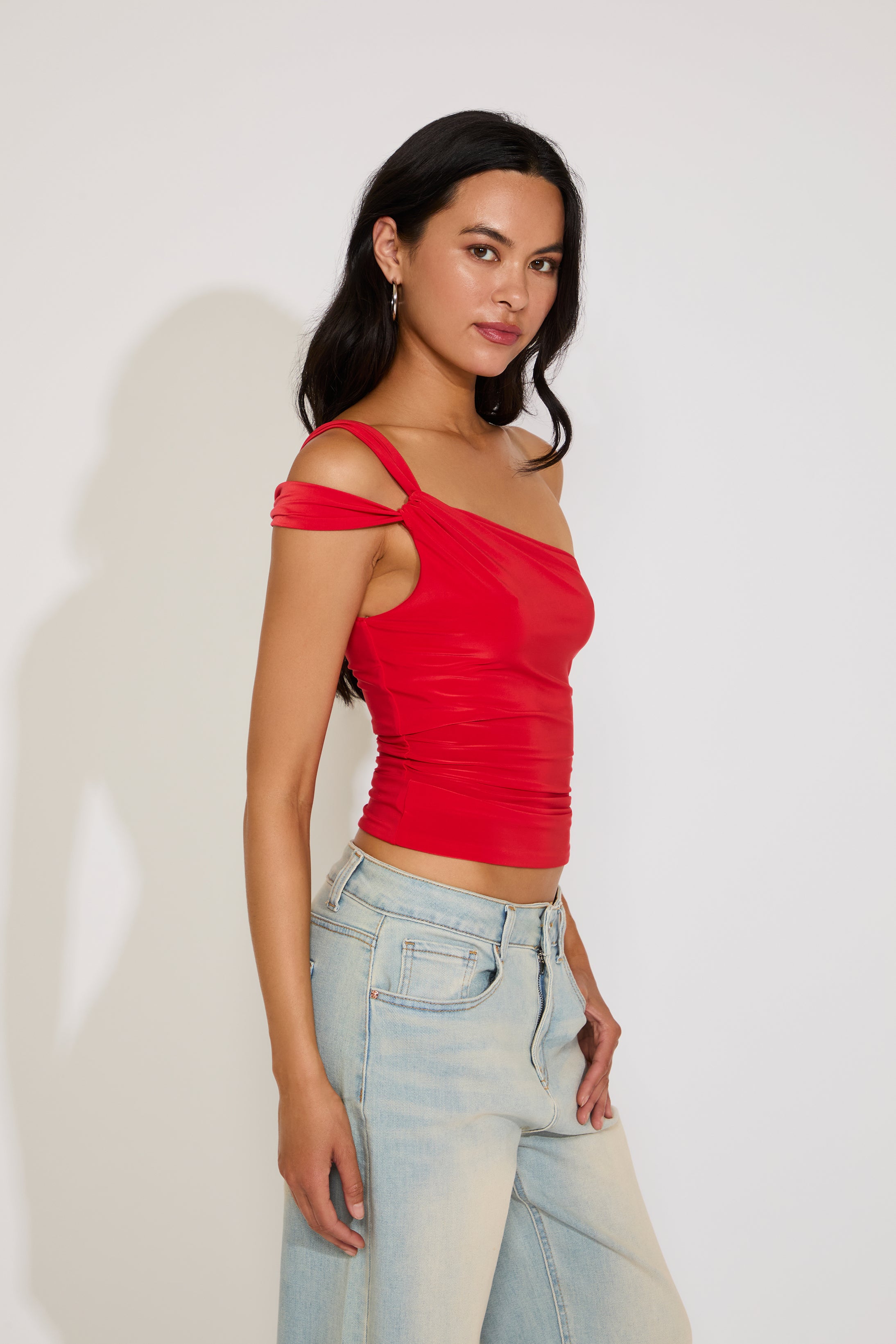 Woman wearing a red top and light blue jeans against a white background