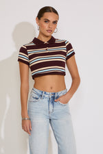 Woman wearing a striped polo shirt and jeans against a plain background