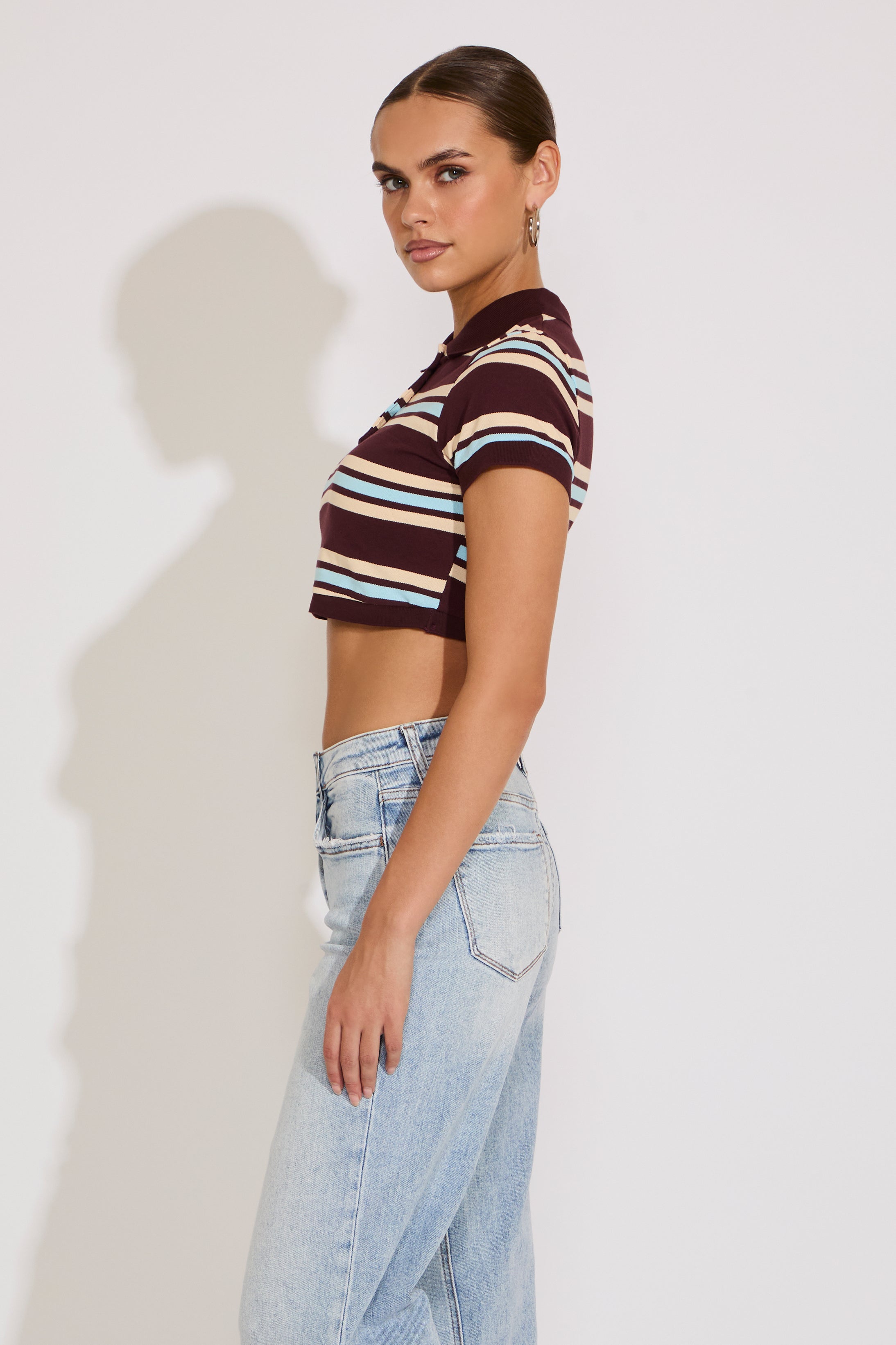 Woman wearing a striped crop top and light blue jeans against a white background