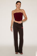 Woman wearing a strapless burgundy top and brown pants with a red logo on a white background