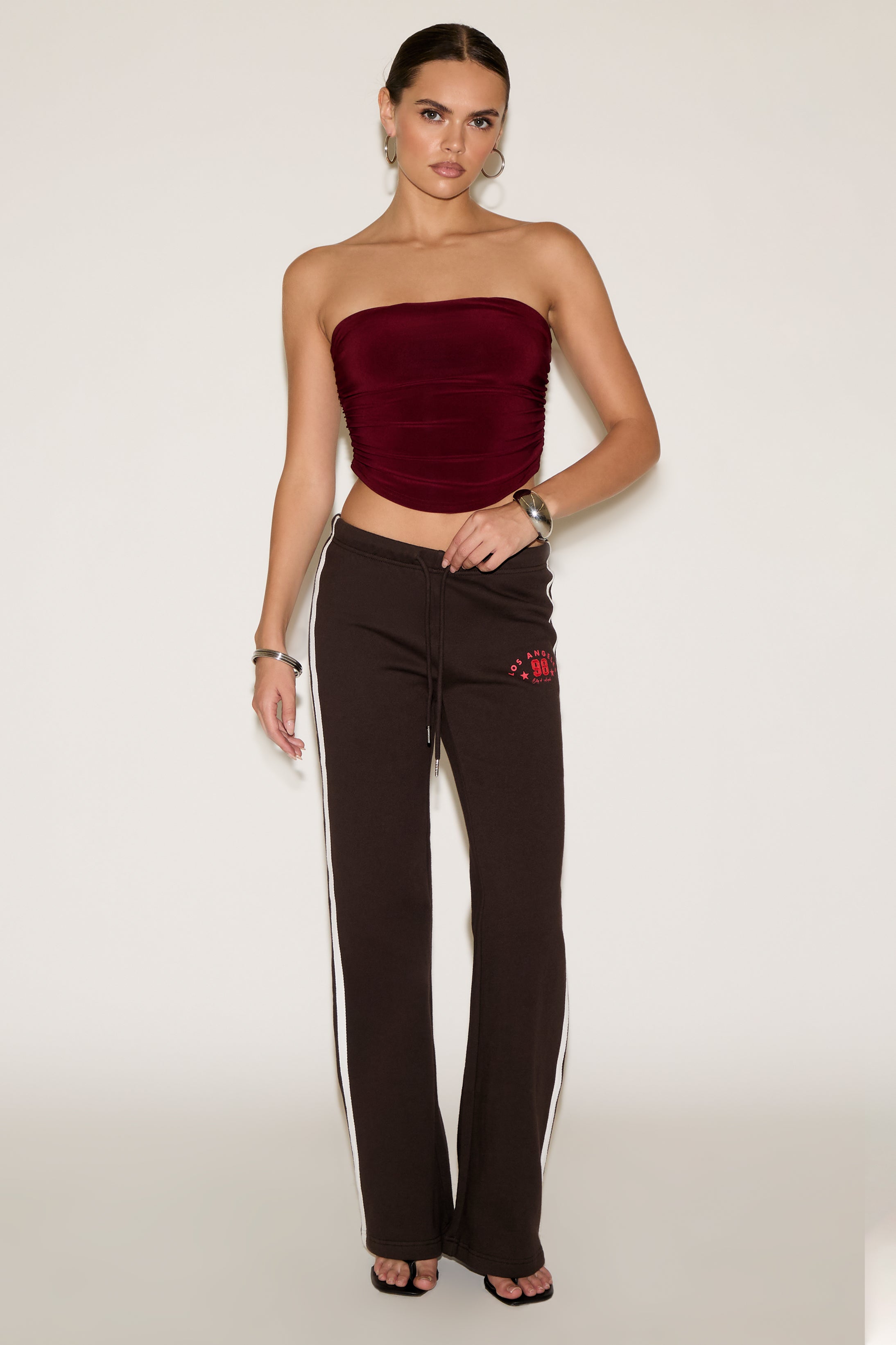 Woman wearing a strapless burgundy top and brown pants with a red logo on a white background