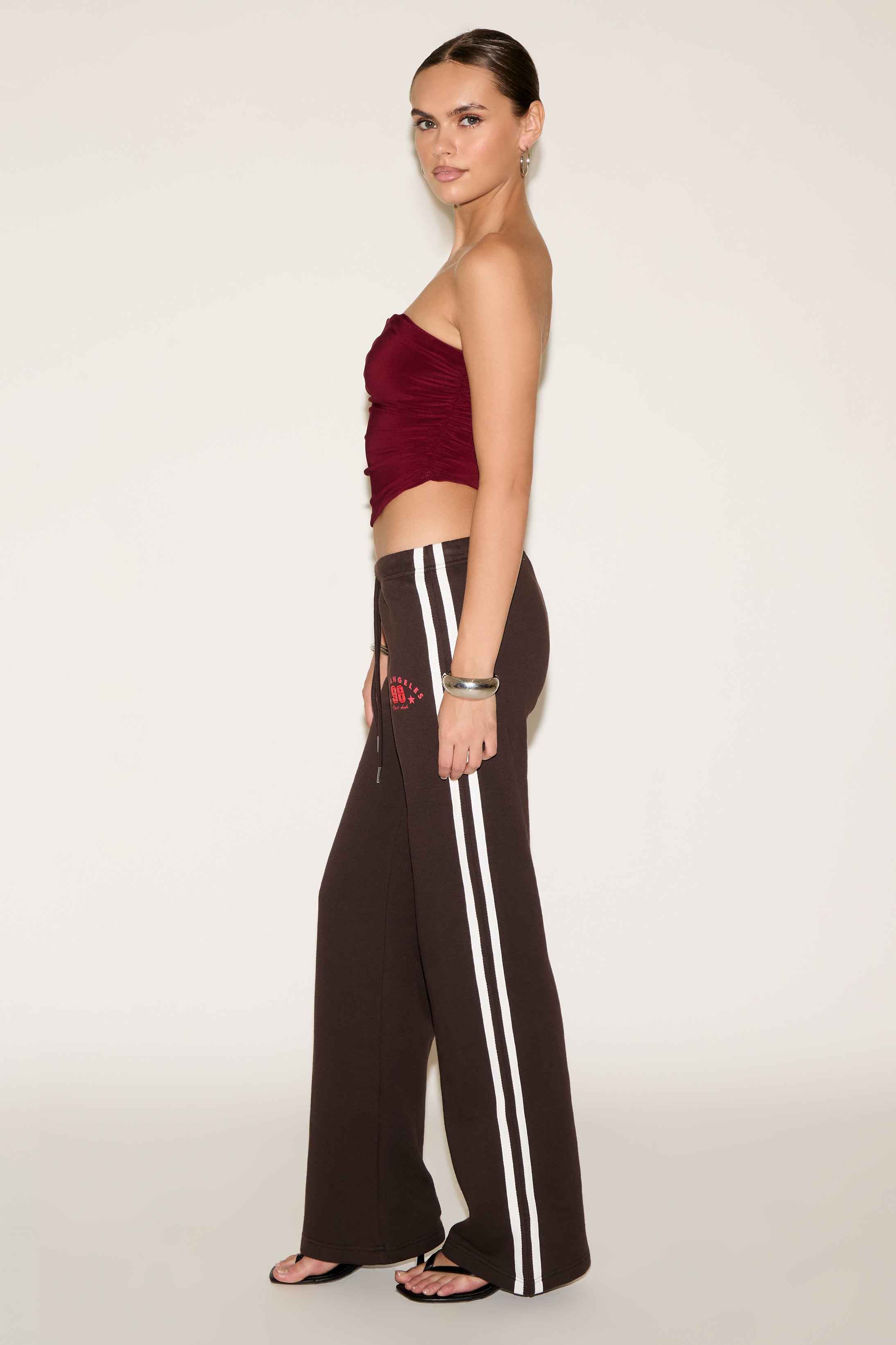Woman wearing a red top and black pants with white stripes on a beige background