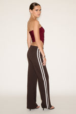 Woman wearing a strapless red top and brown pants with white stripes on a plain background