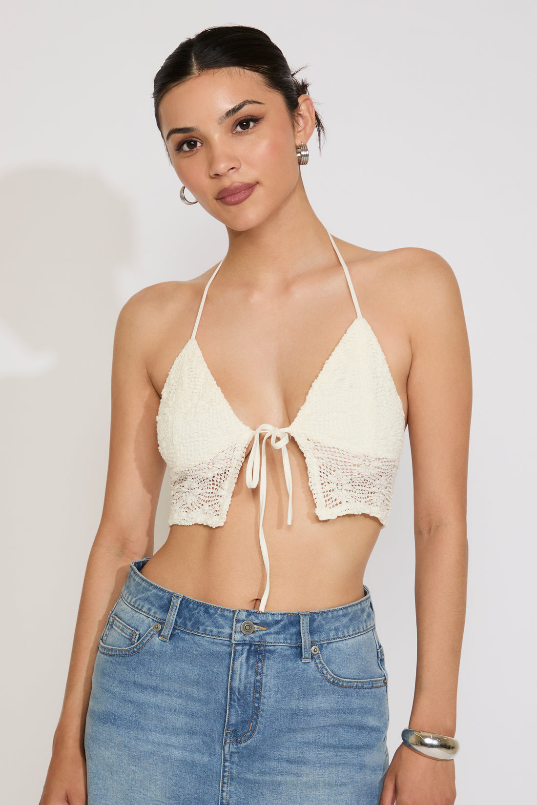 Woman wearing a beige lace halter top and blue jeans on a plain background