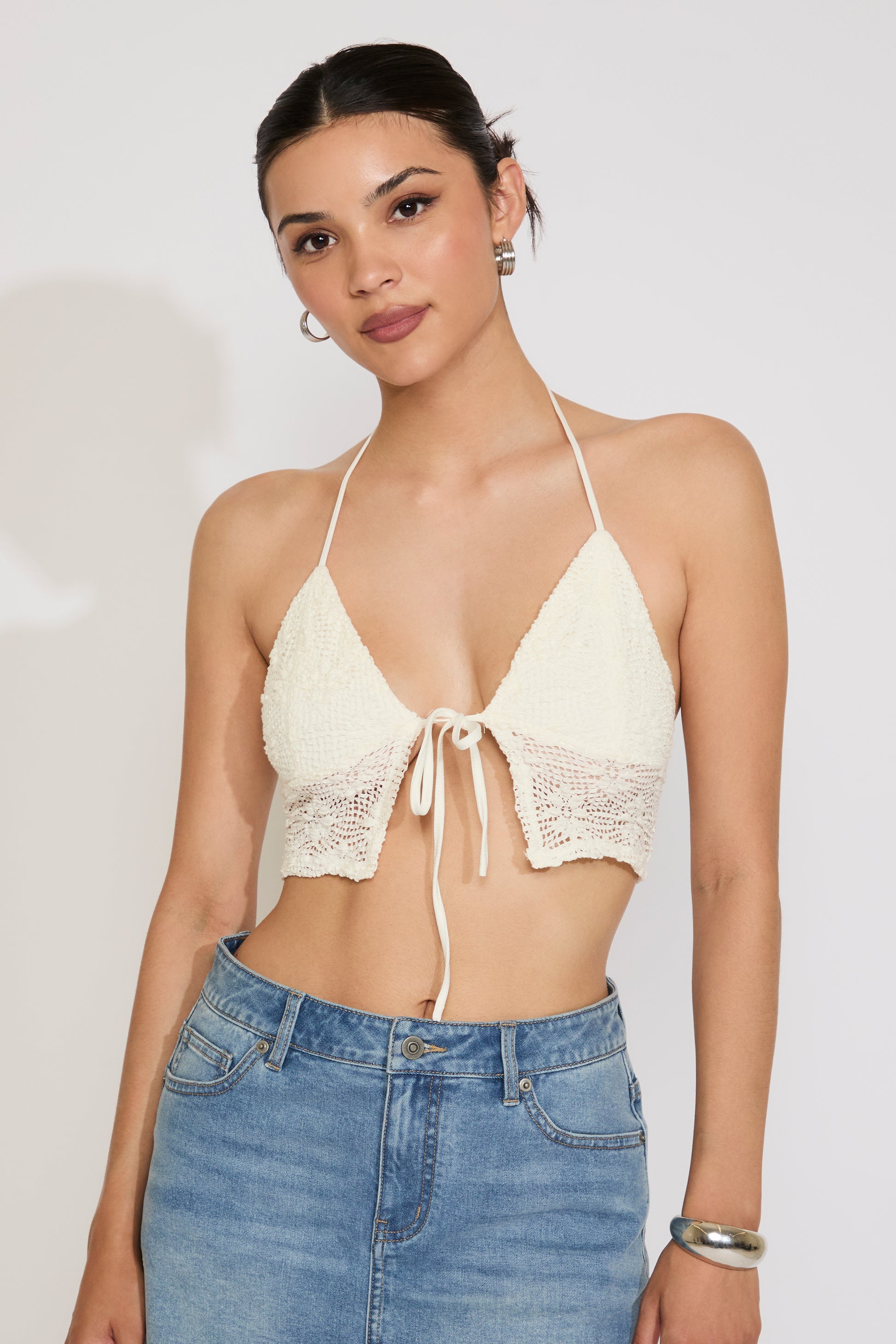 Woman wearing a beige lace halter top and blue jeans on a plain background