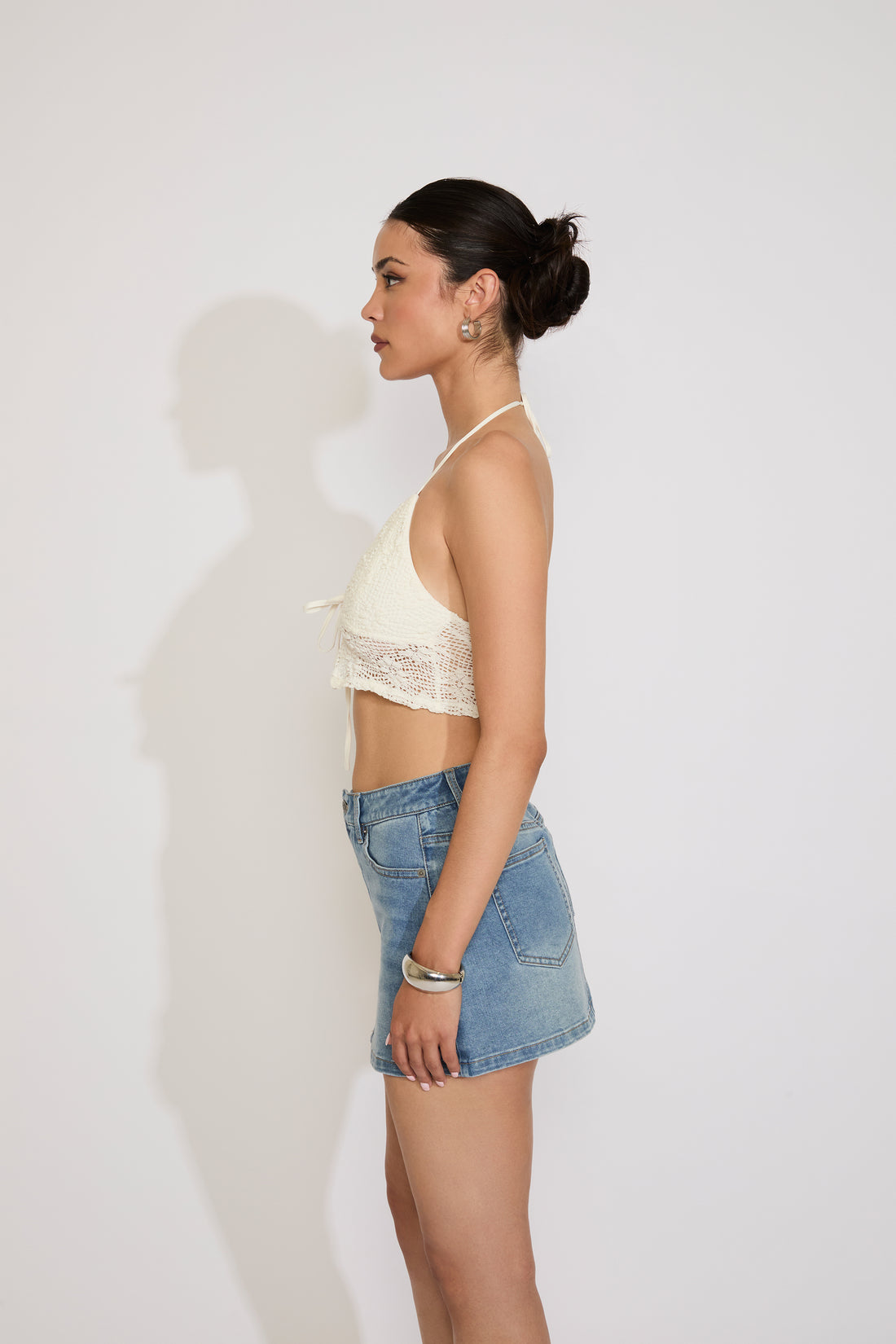 Woman wearing a beige lace halter top and blue jeans on a plain background